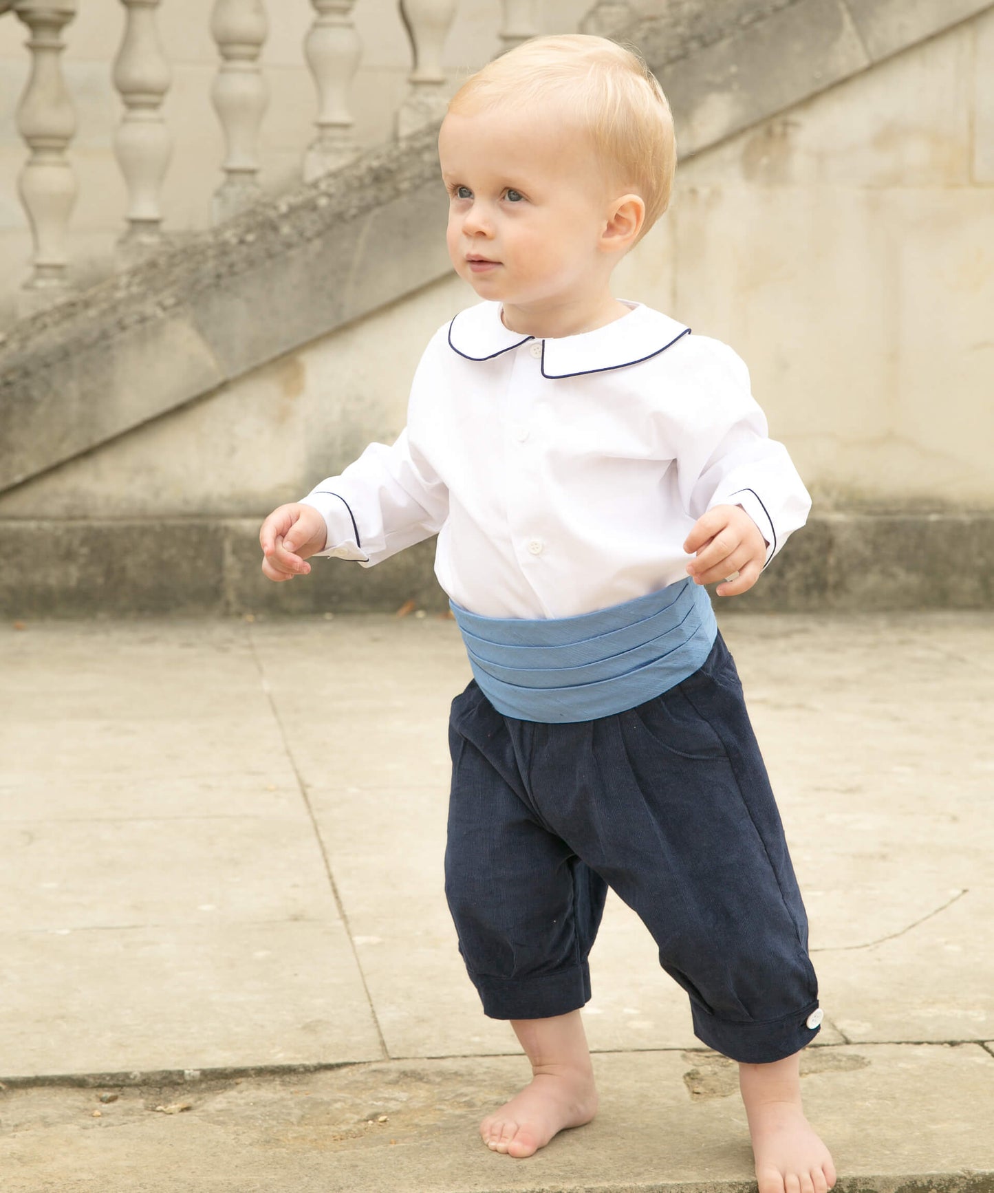 Toddler pageboy wears white peter pan collar shirt, navy knickerbockers and blue silk cummerbund